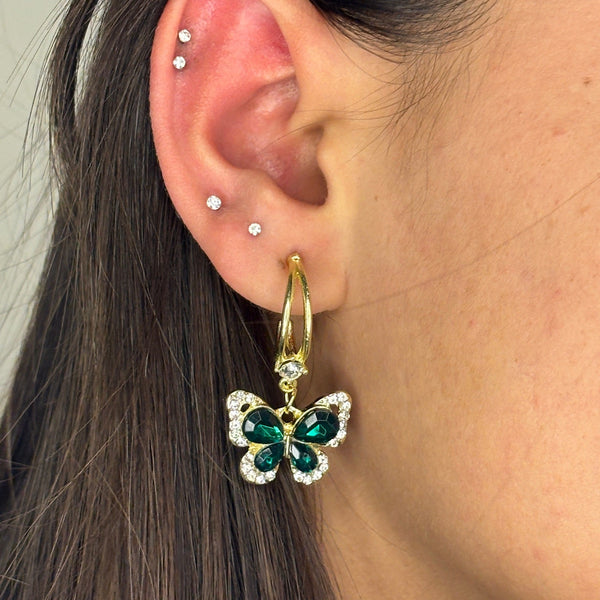 Butterfly earring with green gemstones worn by a person with dark hair.