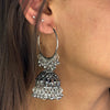 Close-up of a person wearing silver hoop earrings with intricate designs.