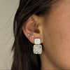 Close-up of a person wearing a square earring with a clear gemstone.