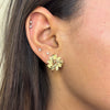 Close-up of an ear wearing a gold flower-shaped earring with a neutral background