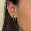 Close-up of an ear with gold hoop earrings and multiple small stud earrings.