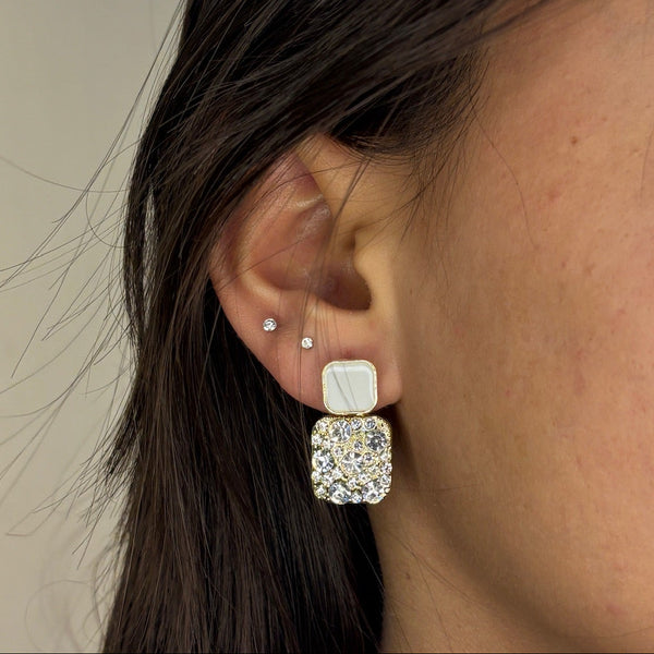 Close-up of a person wearing a square earring with a clear gemstone.